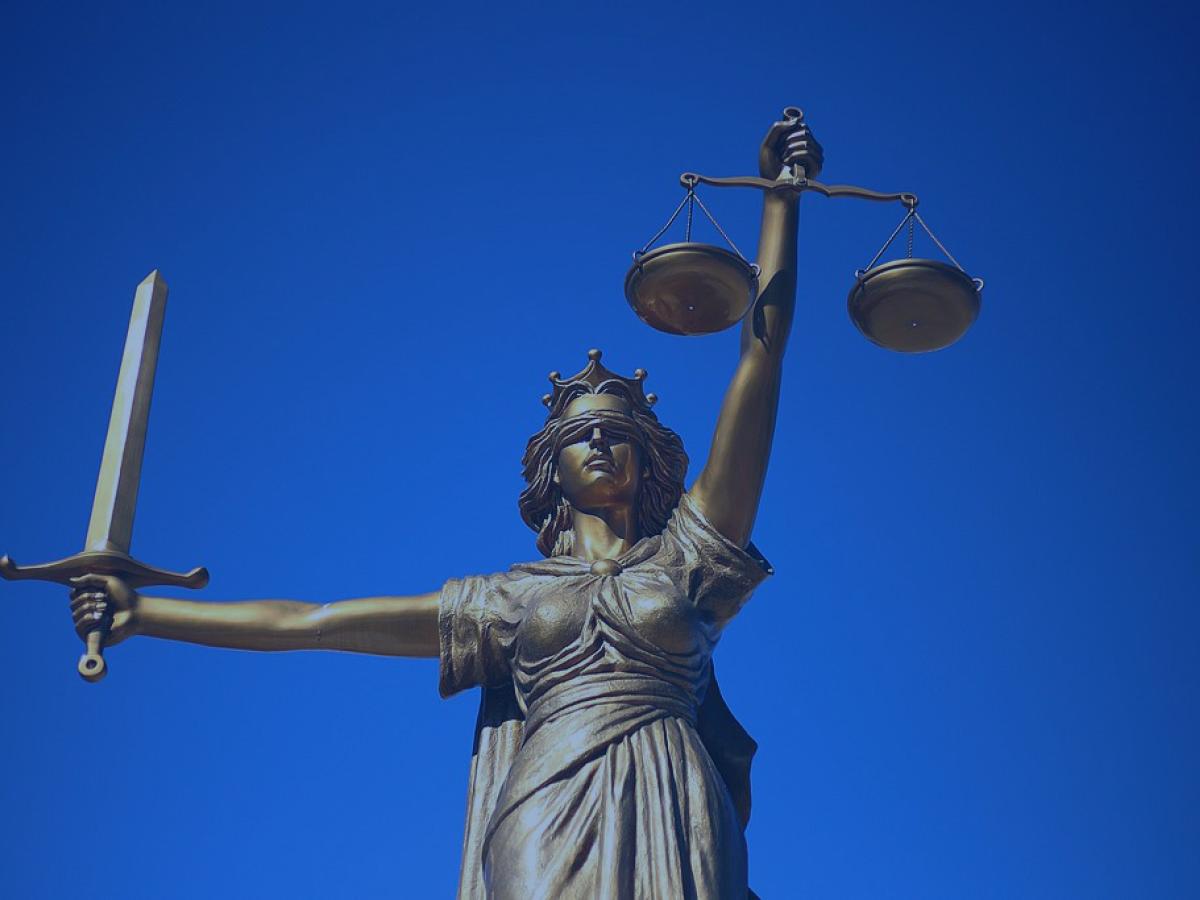 A statue of Justice holds a sword aloft in one hand, and set of scales in the other.