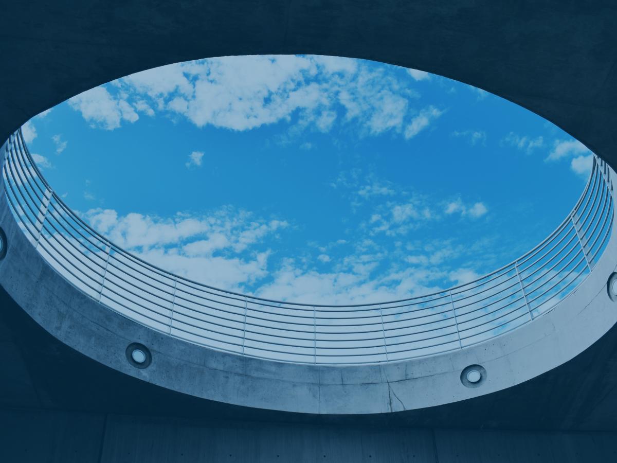 A cloud-dappled s blue sky is viewed through a large circular opening, from below.