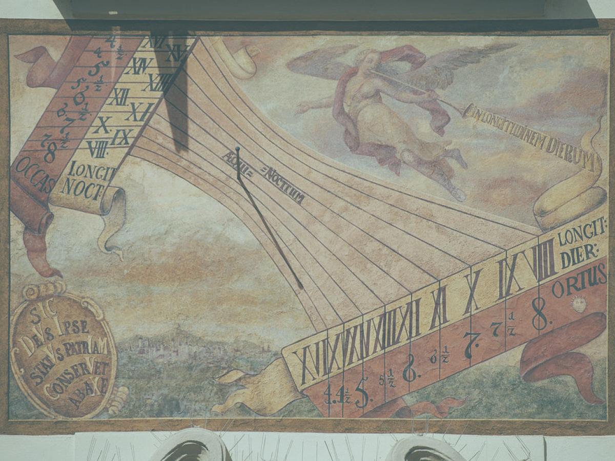 A sundial on a wall casts a small shadow on a painted list of numbers and symbols