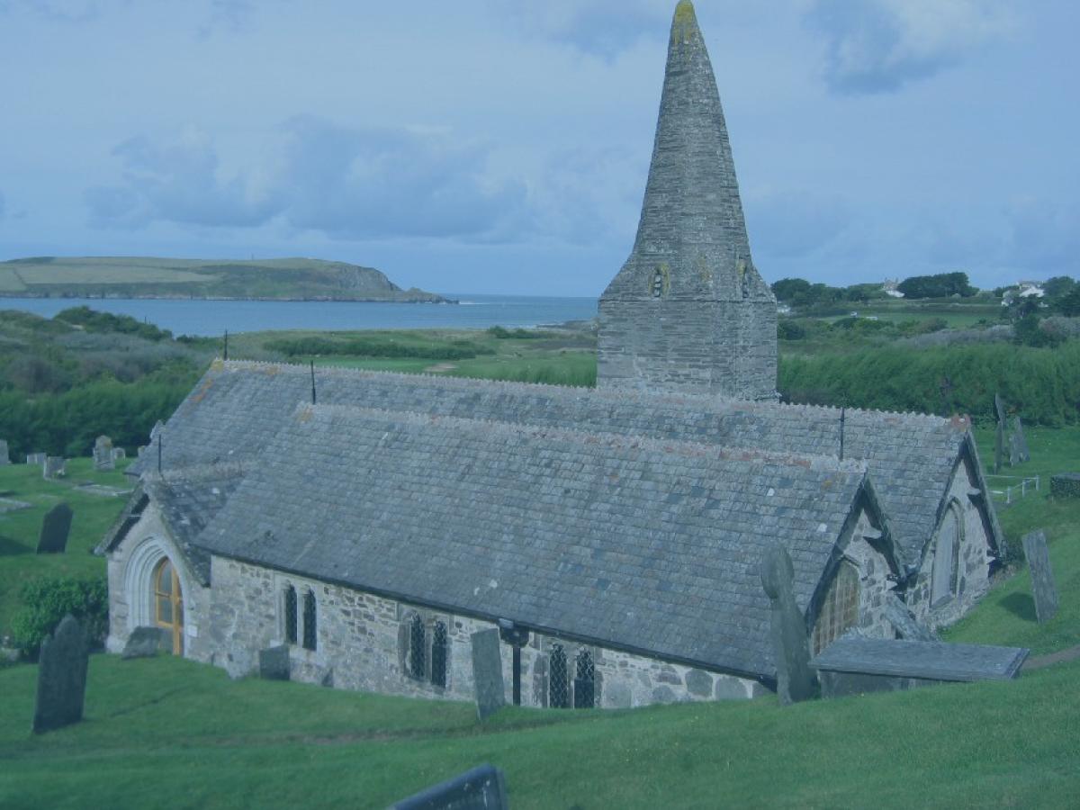 A stone church and tower emerge from the hillside with the sea in the distance.