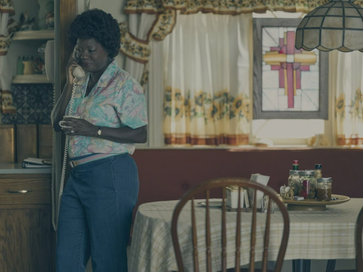 A woman stands in a kitchen diner hold a phone with a cord.