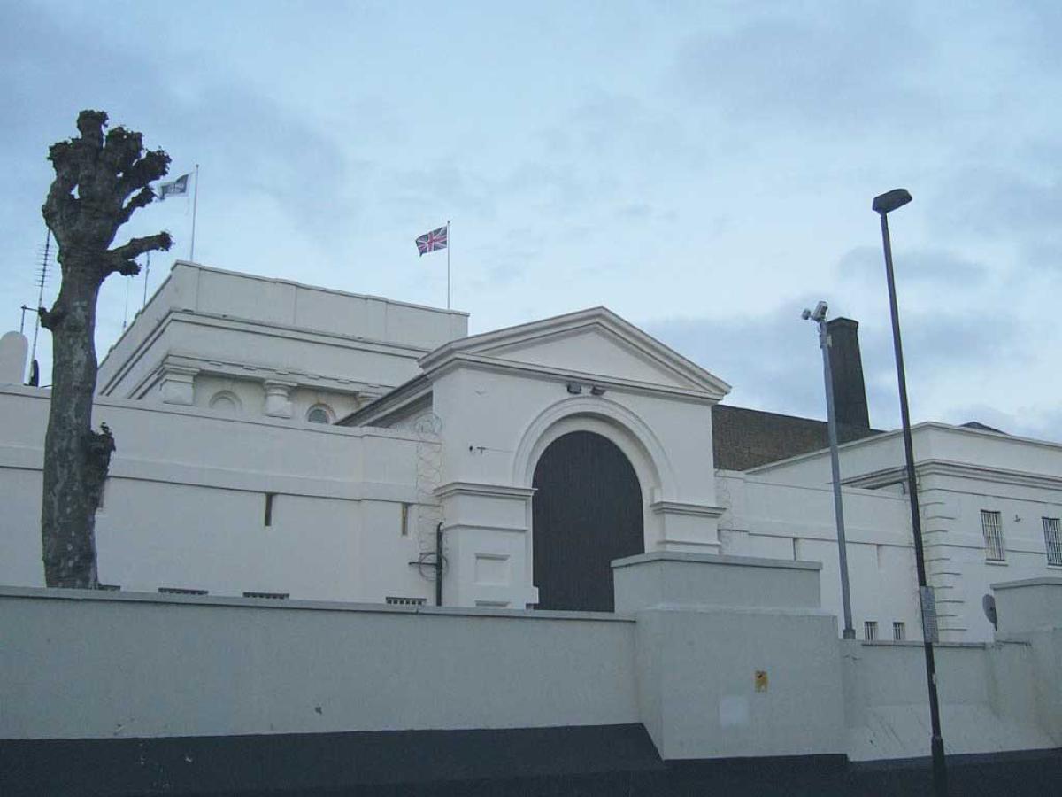 An arched gateway to a prison sits behind a low raised wall. No windows are visible