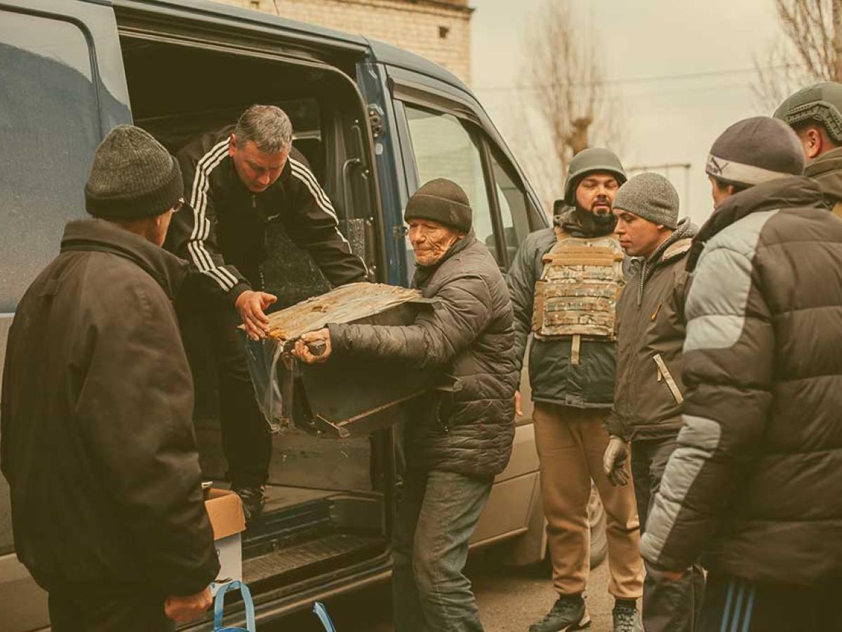 People help unload aid parcels from the side of a van, some wearing body armour.