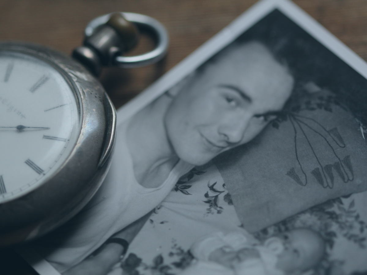 A pocket watch rests next to a black and white photograph of a father lying beside a new born baby.