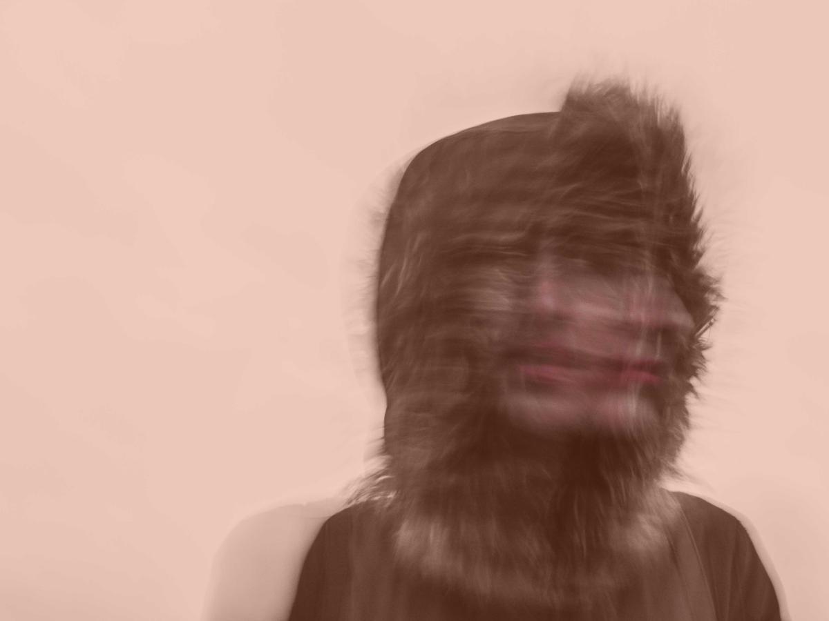 A blurred exposure of a person under a hood turning their head to the side.