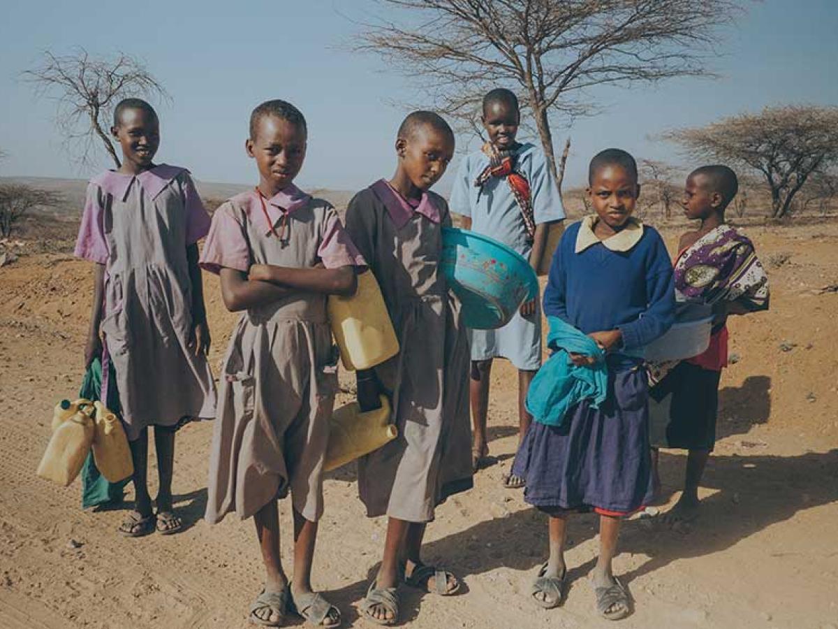 Girls stand in the northern Kenyan scrubland holding water bottles.