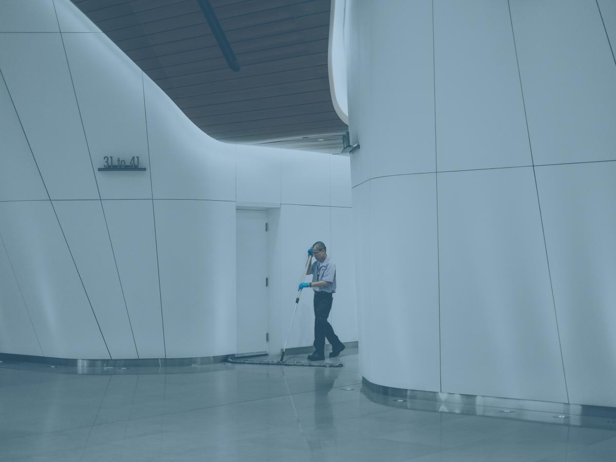 A cleaner sweeps between large white interior walls of a concourse.