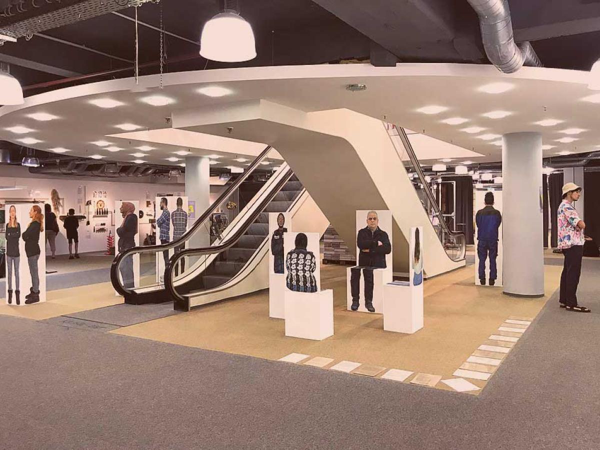 Between and around two escalators in a library, stand paintings of different people.