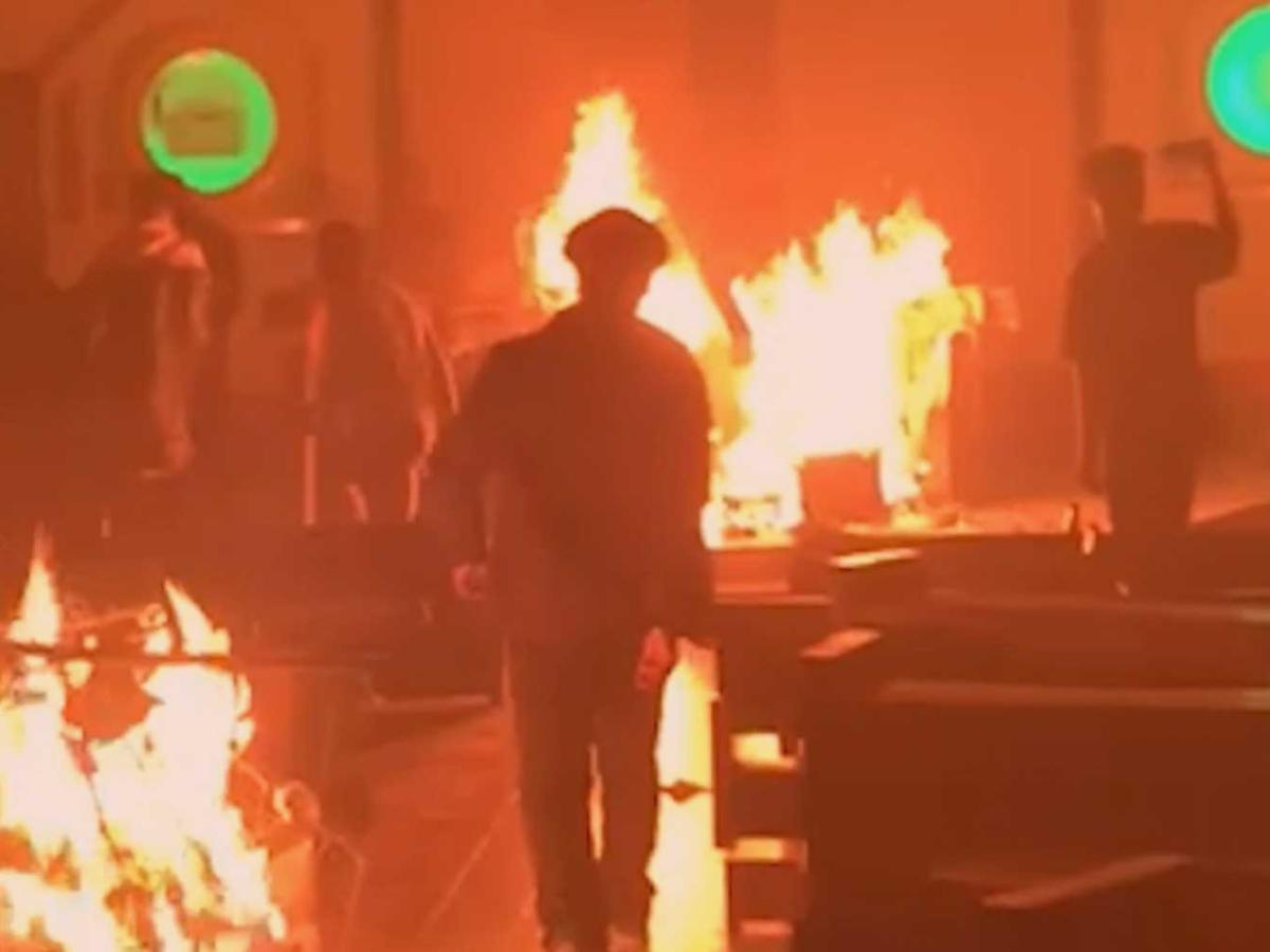 A church interior glowing red as parts of its furniture burn. A man walks down the aisel