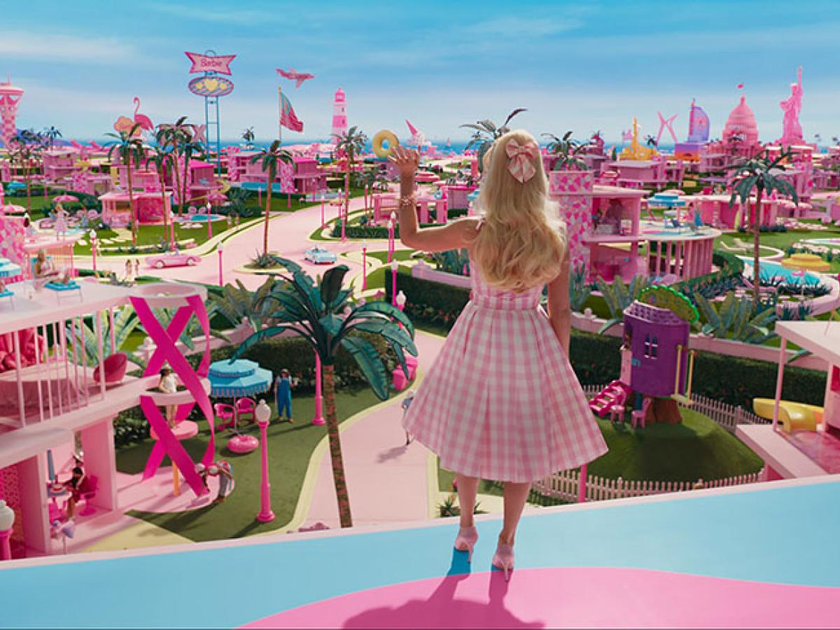 Barbie stands on a balcony and waves while looking out over her city.