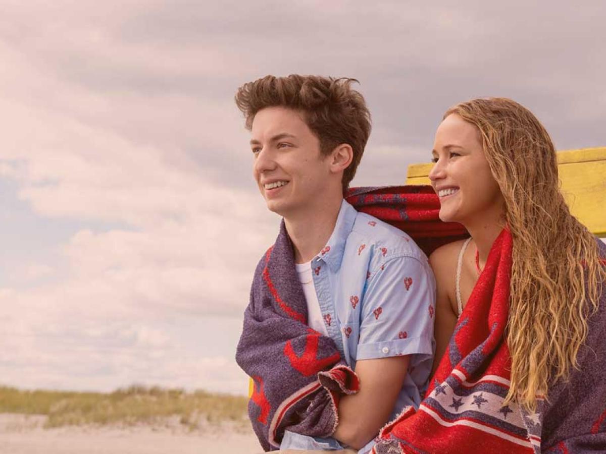 A young couple sit next to each other on a beach sharing a towel.