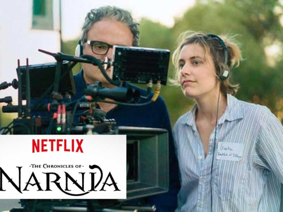 A film director stands next to a camera to look at its screen, while a camera operator looks on