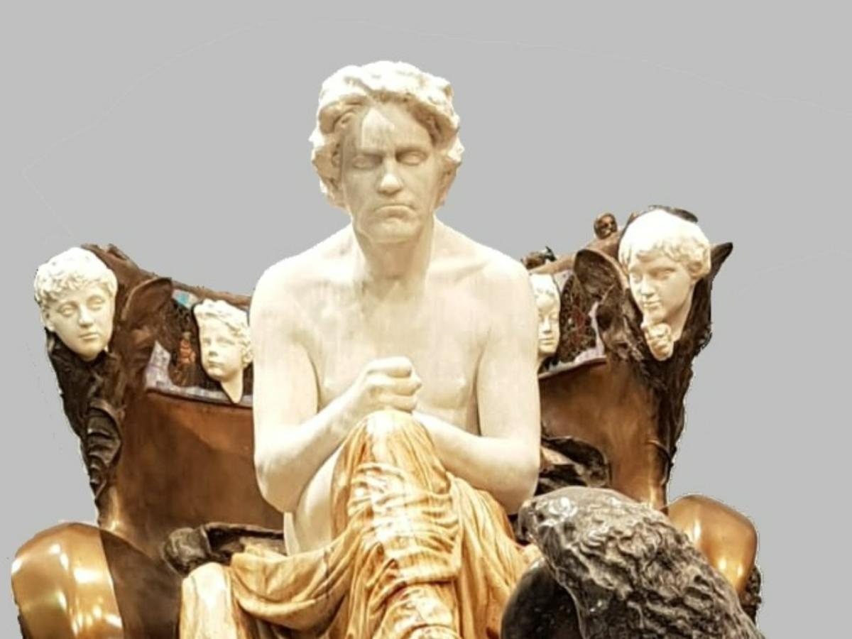 Agrand statue of Beethoven as a classical hero seats him on a throne on a dias.