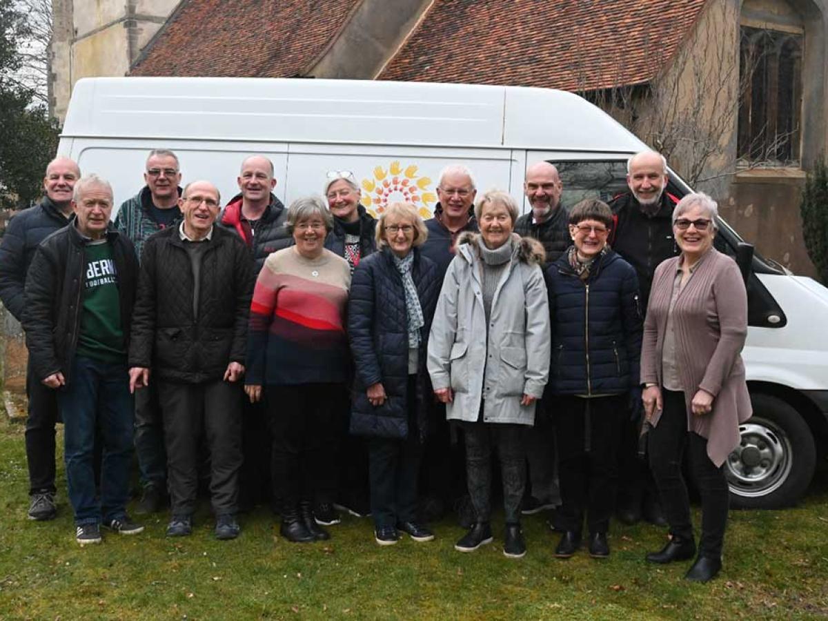 A group of people stand in front of the side of a van marked 'Furniture Friends.