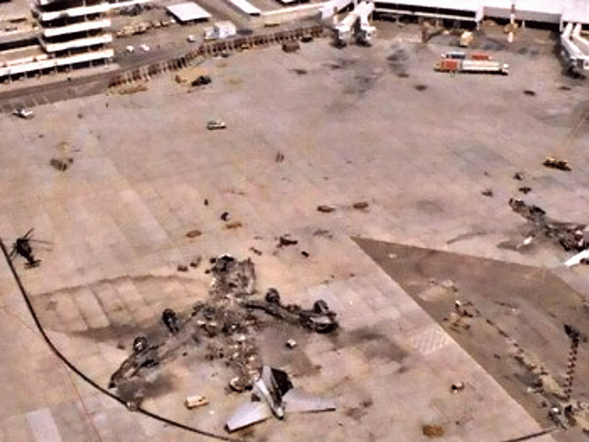 A destroyed airliner lies on the apron of a war-torn airport.