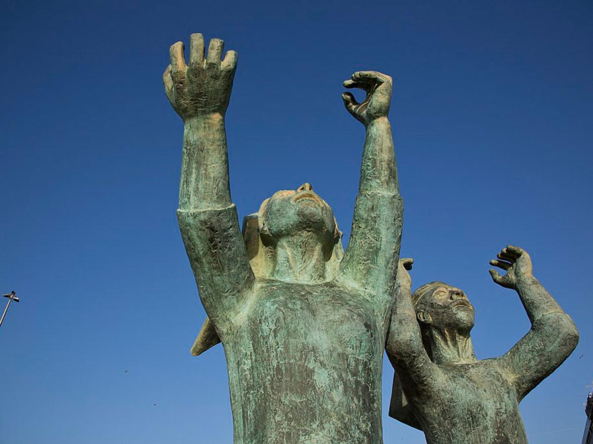 A sculpture shows mourning women raising hands and fists to the sky.