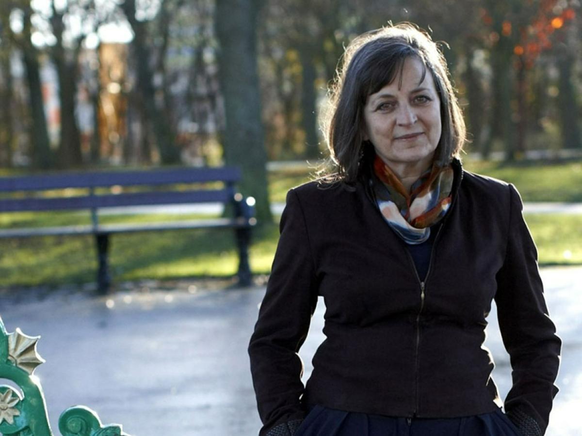 A woman stands in an autumnal-looking park, with her hands in her pockets