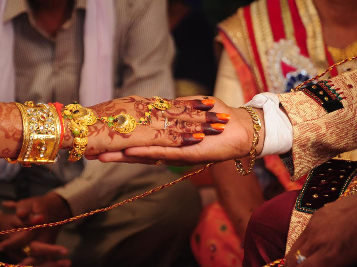 A close-up of a bride groom holding the brides hand. Her hand is henna tattooed and bears gold rings and bracelets.