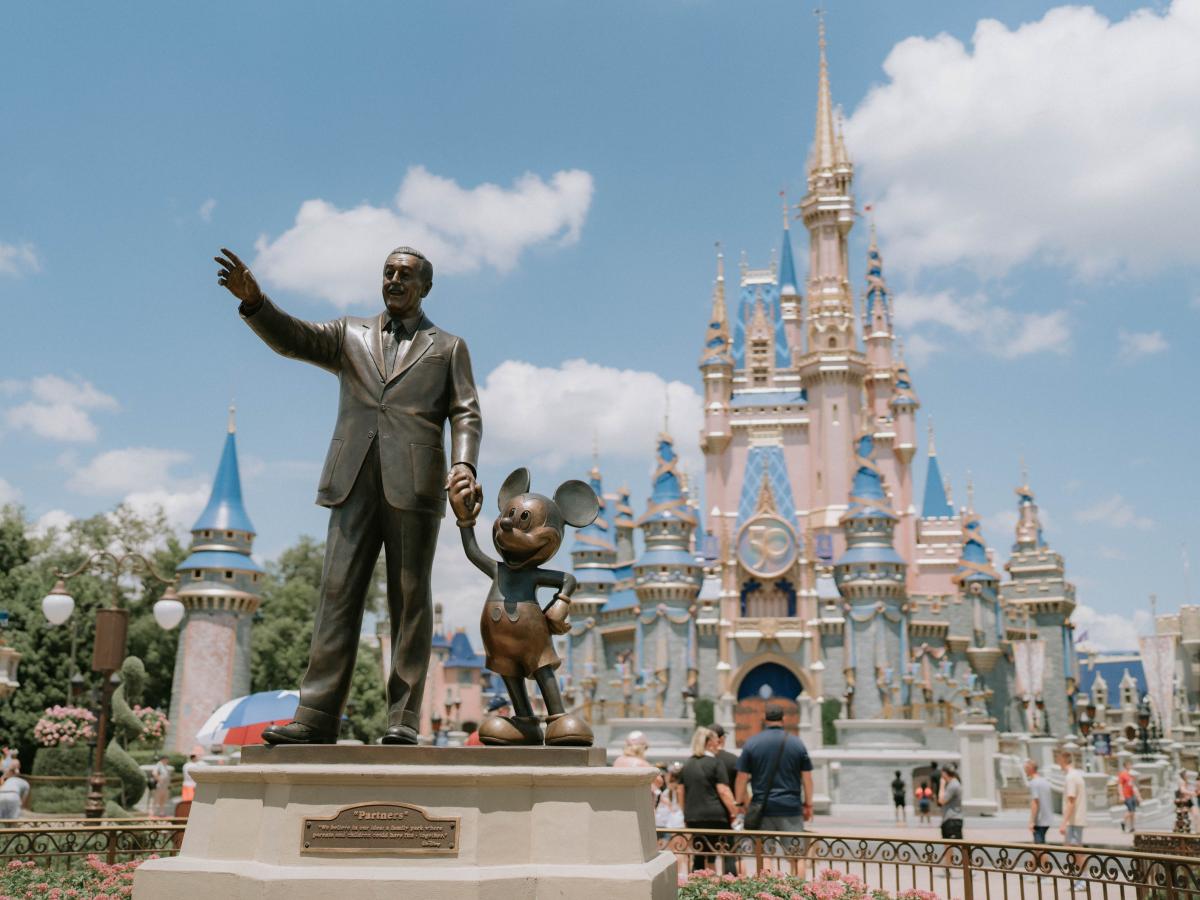 A statue of Walt Disney holding hands with Mickey Mouse in front of Cinderella's Castle