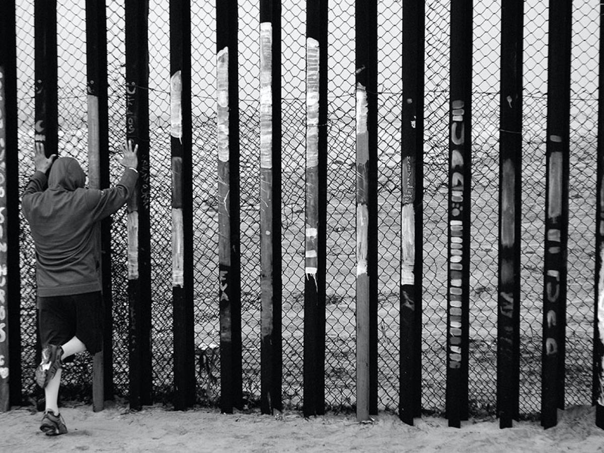 A person holds the vertical tall steel bars of a border fence.