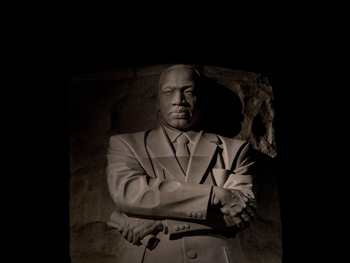 An imposing stone statue of Martin Luther King standing with his arms crossed.