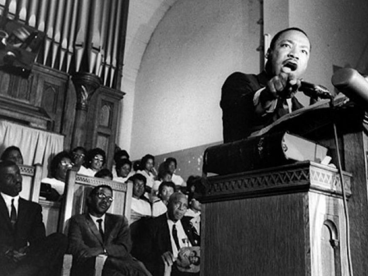 Martin Luther King reaches from the pulpit of a church while he preaches.