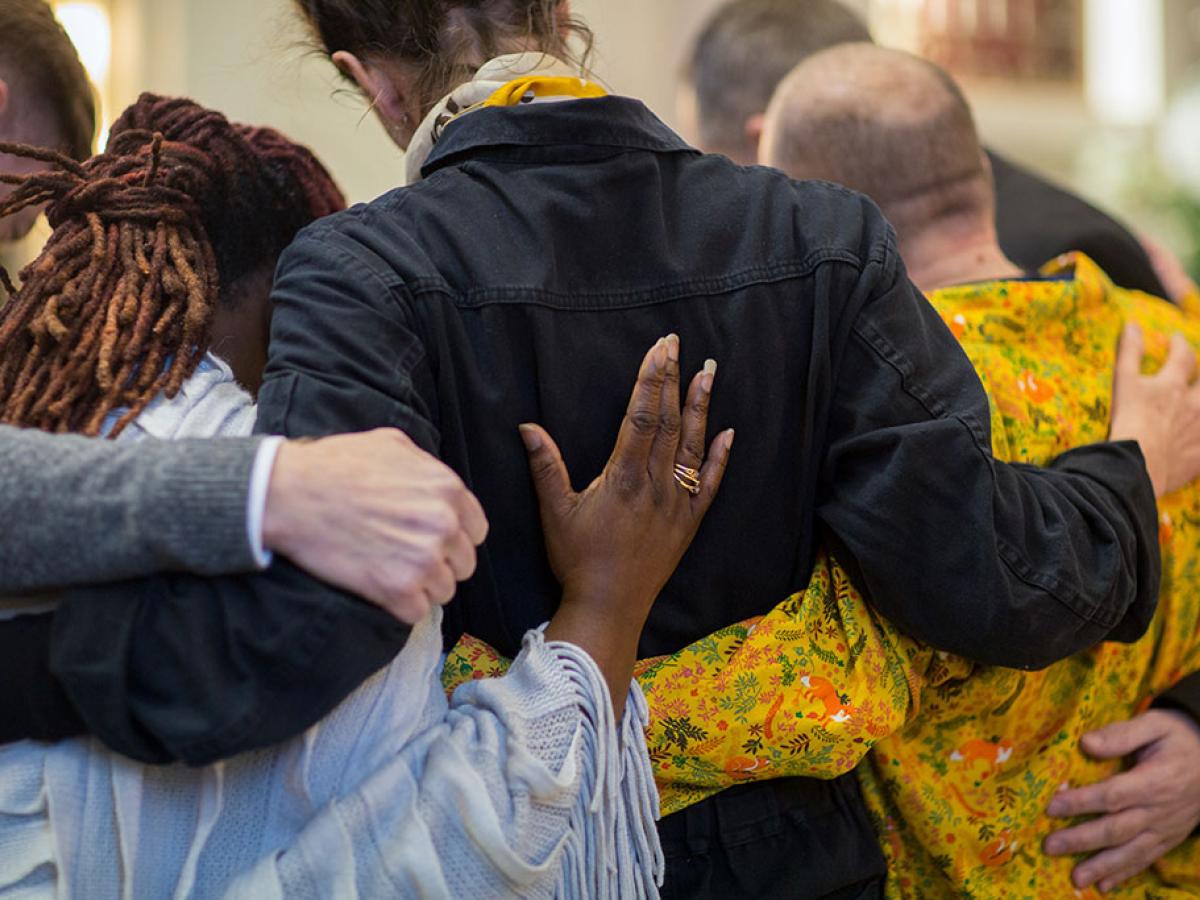 A group of grieving friends with their hands on each others backs.