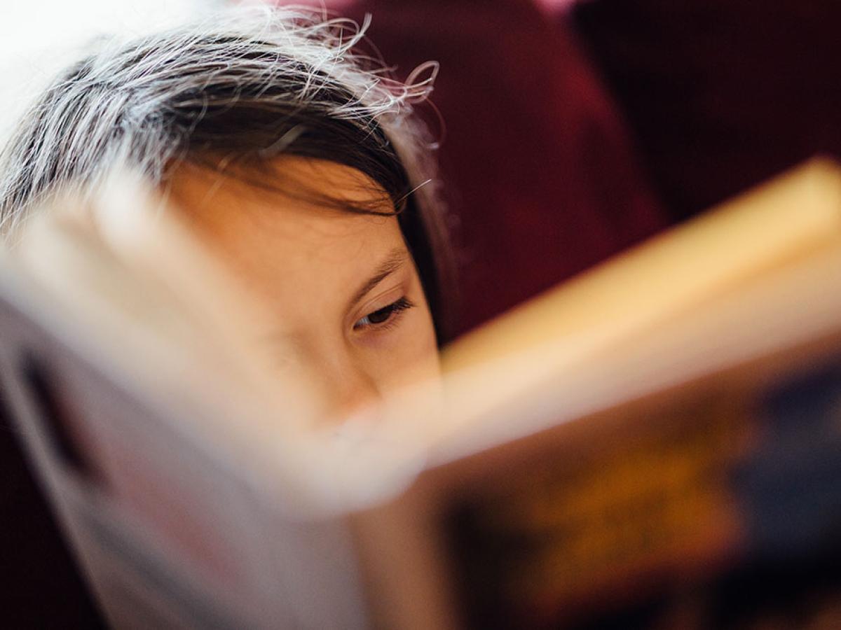 A close up of face, showing an eye, mostly obscured by a closely-held open book.