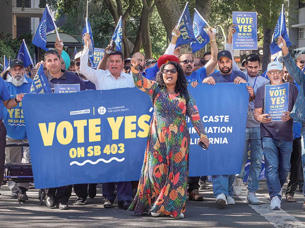 A group of protesters march behind a banner waving flags.