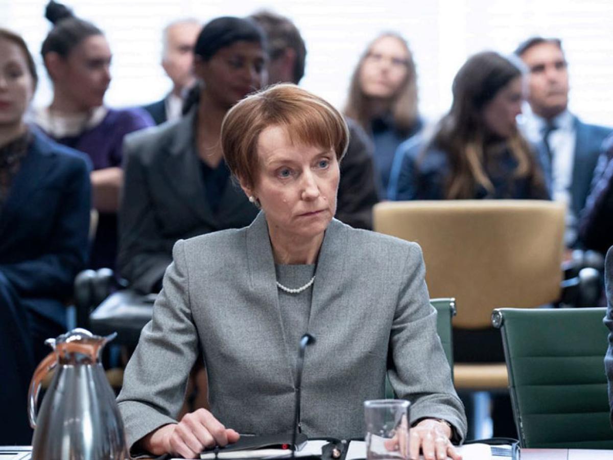 A tense-looking woman, sitting at  desk, stares into the middle disance.