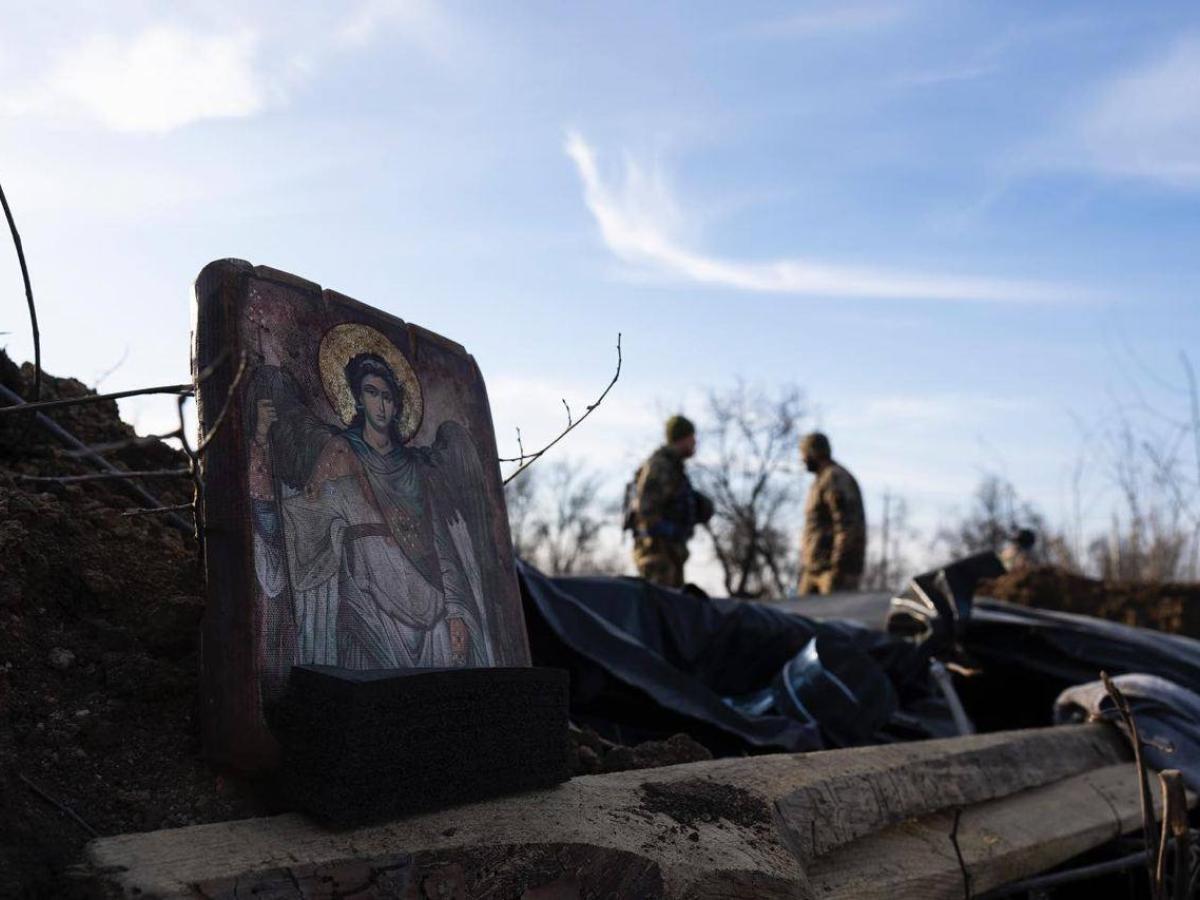 A religious icon is propped on the side of a trench, a soldier can be seen further down the trench.