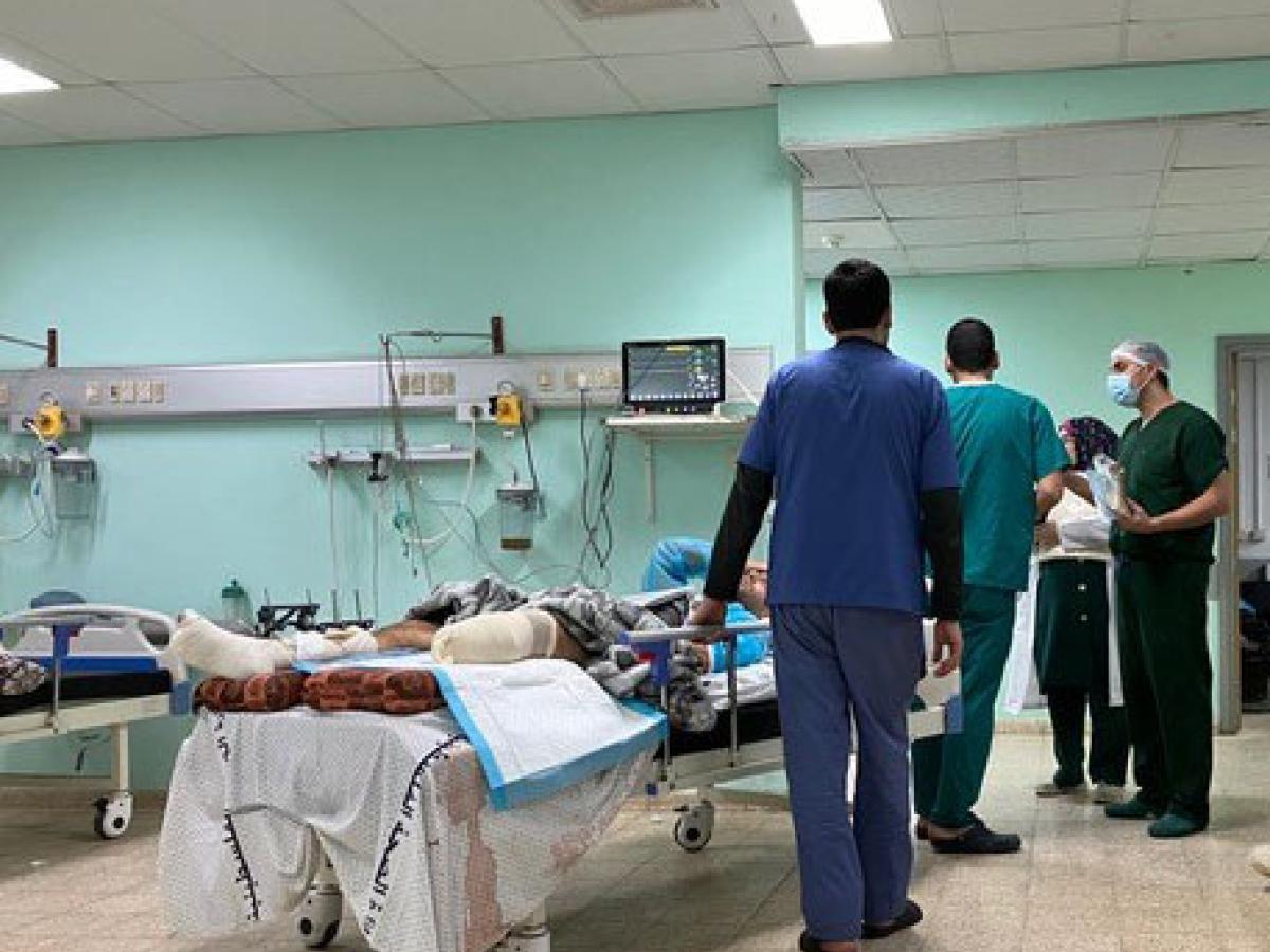 Medical staff stand beside a bed in which a man lies with an amputated leg.