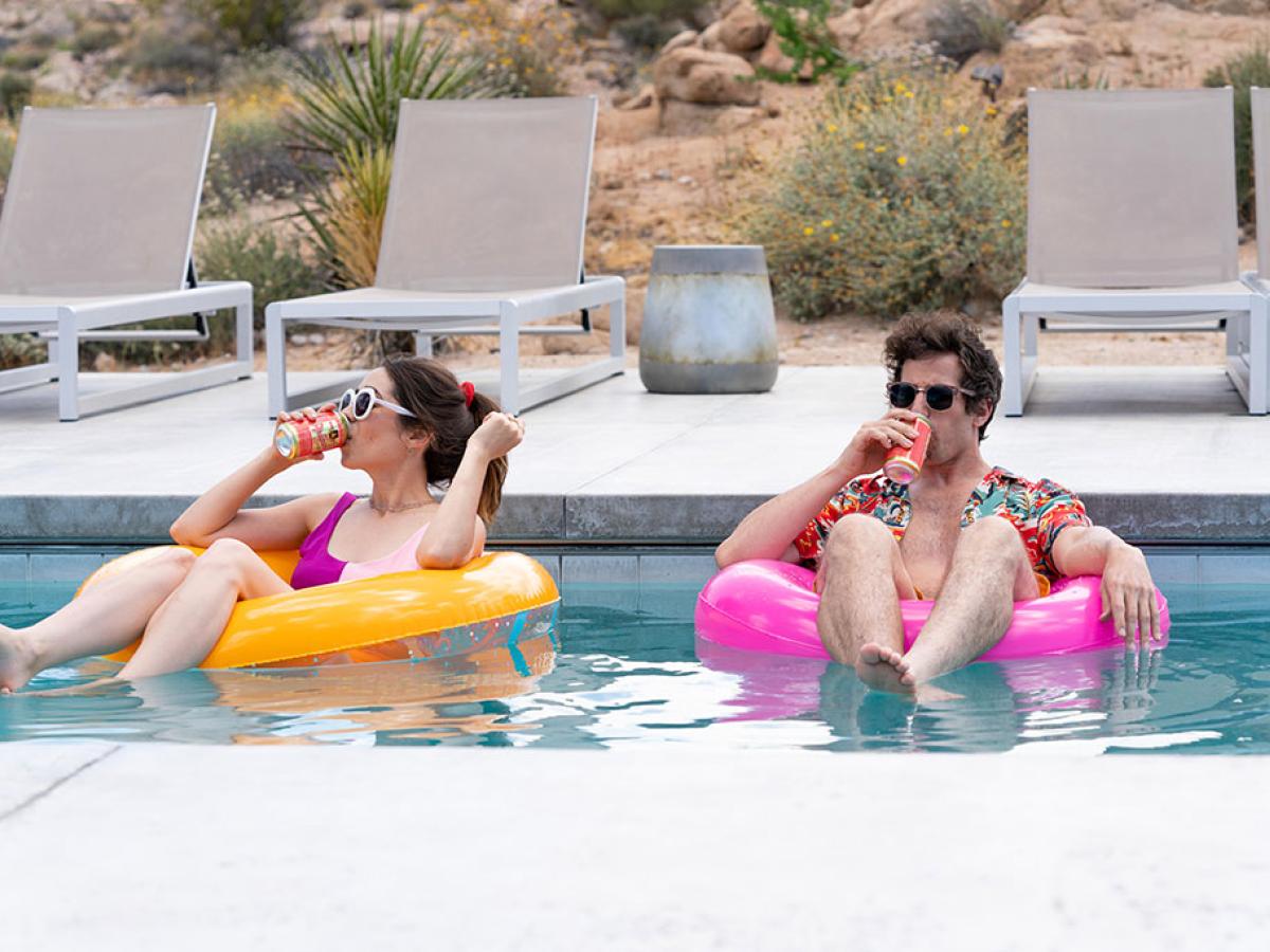 A young couple lounge on floating rings in a swimming pool.