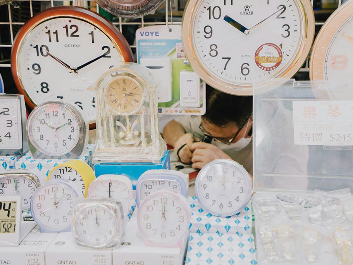 A clock repair peers at a clock he is repairing, amid a see of alarm and wall clocks on display