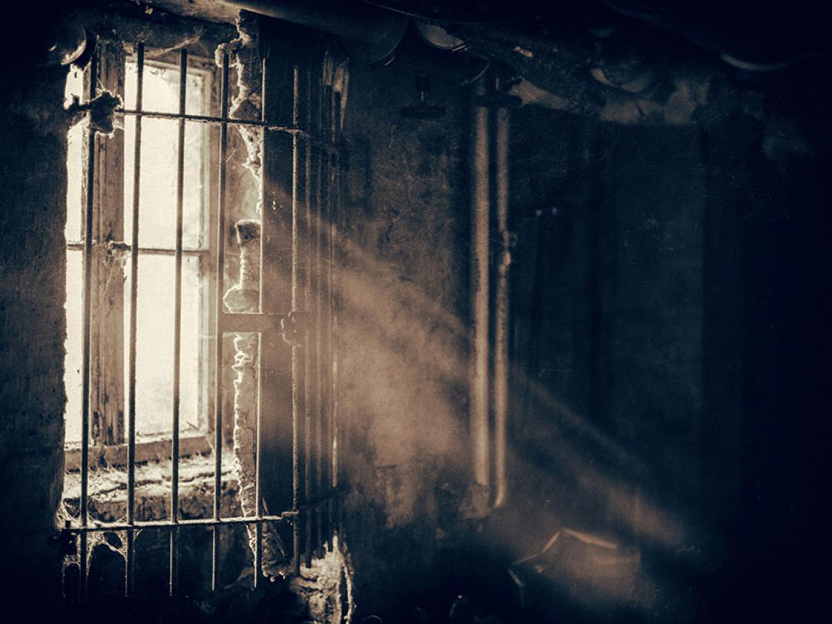 A window sheds light through locked bars into a dusty and dark room,