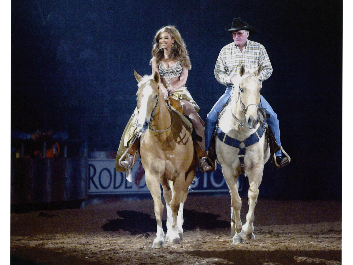 Side by side, two rodeo riders on horses trot toward the camera. One is Beyonce, the other a cowboy