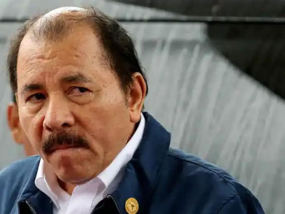 An balding man with a moustache turns to look at a camera.