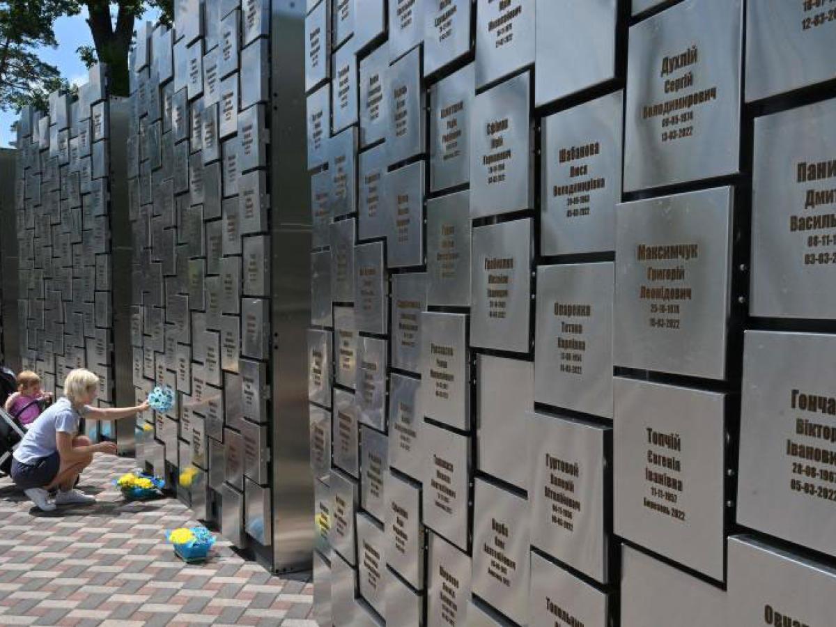 A woman squats and touches a war memorial