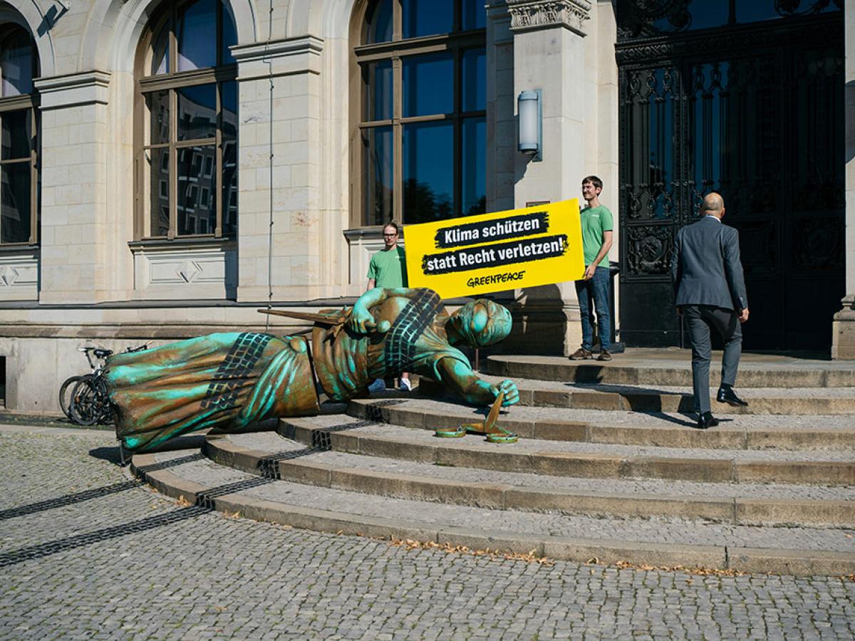 A fallen statute with tyre tracks over it lies on the steps to a government building, in a form of protest.
