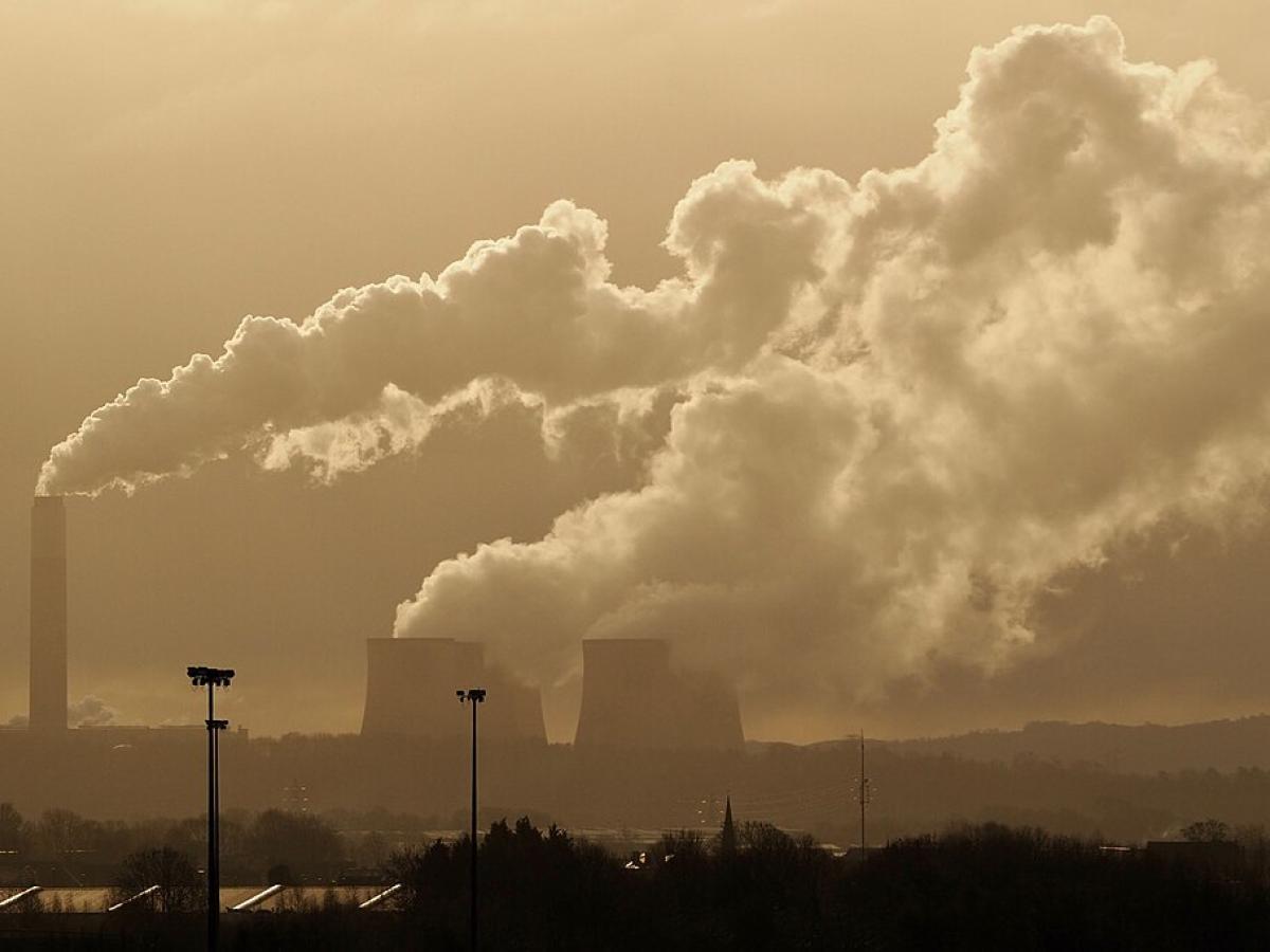 A sky line shows steam rising from a power station's chimney and cooling towers.