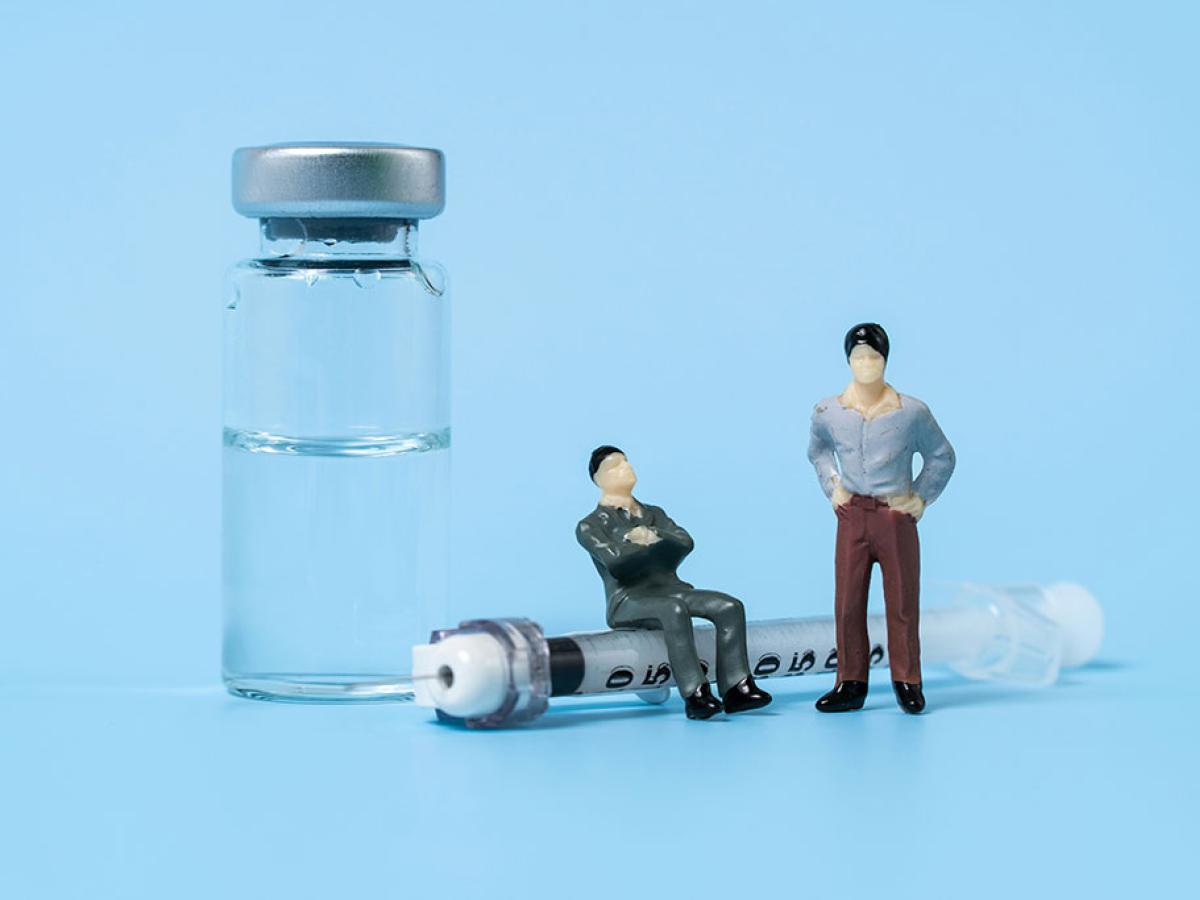 A tableau shows minature figures of two people, one sitting on a life size syringe and the other stands