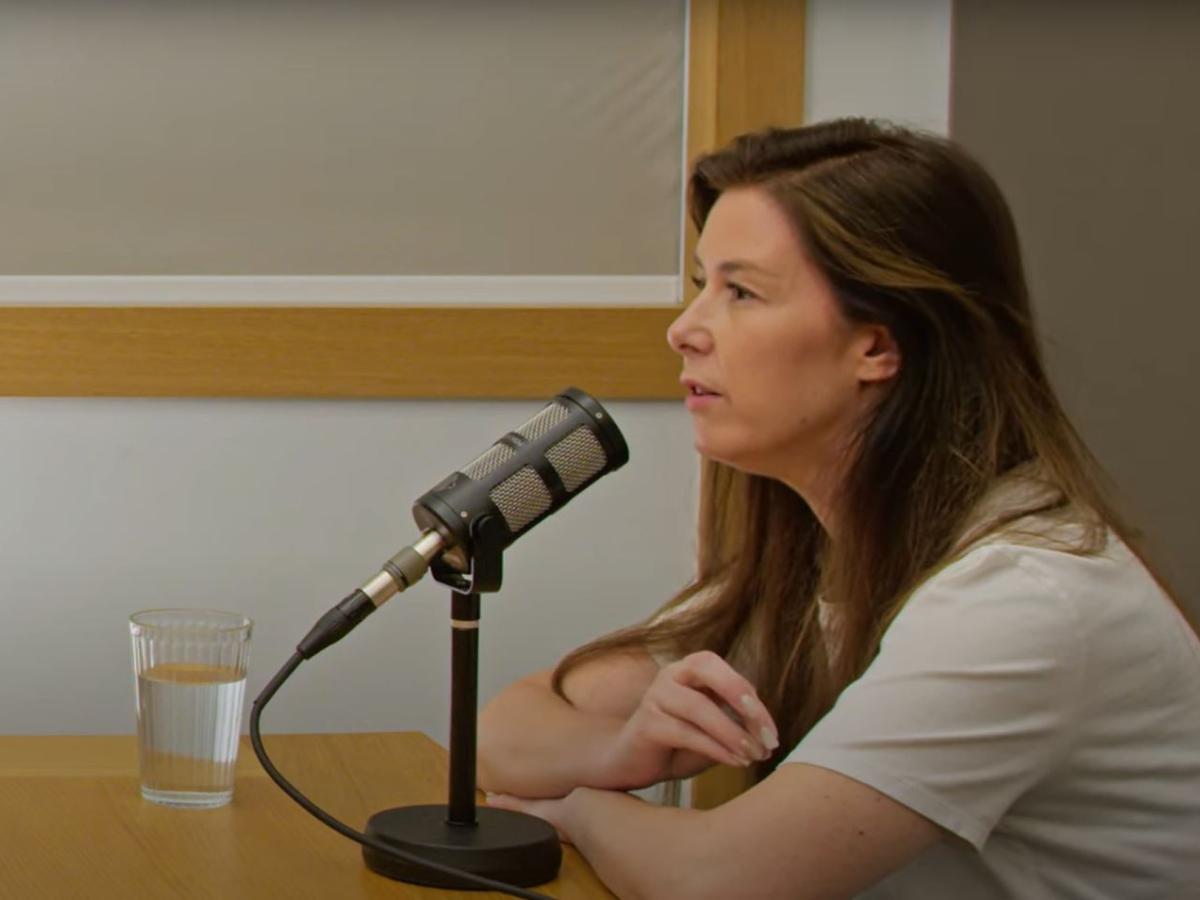 A woman leans on a table, talking into a microphone.