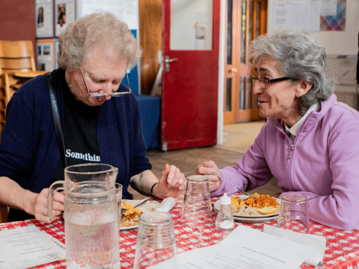 two women sit a table chatting.