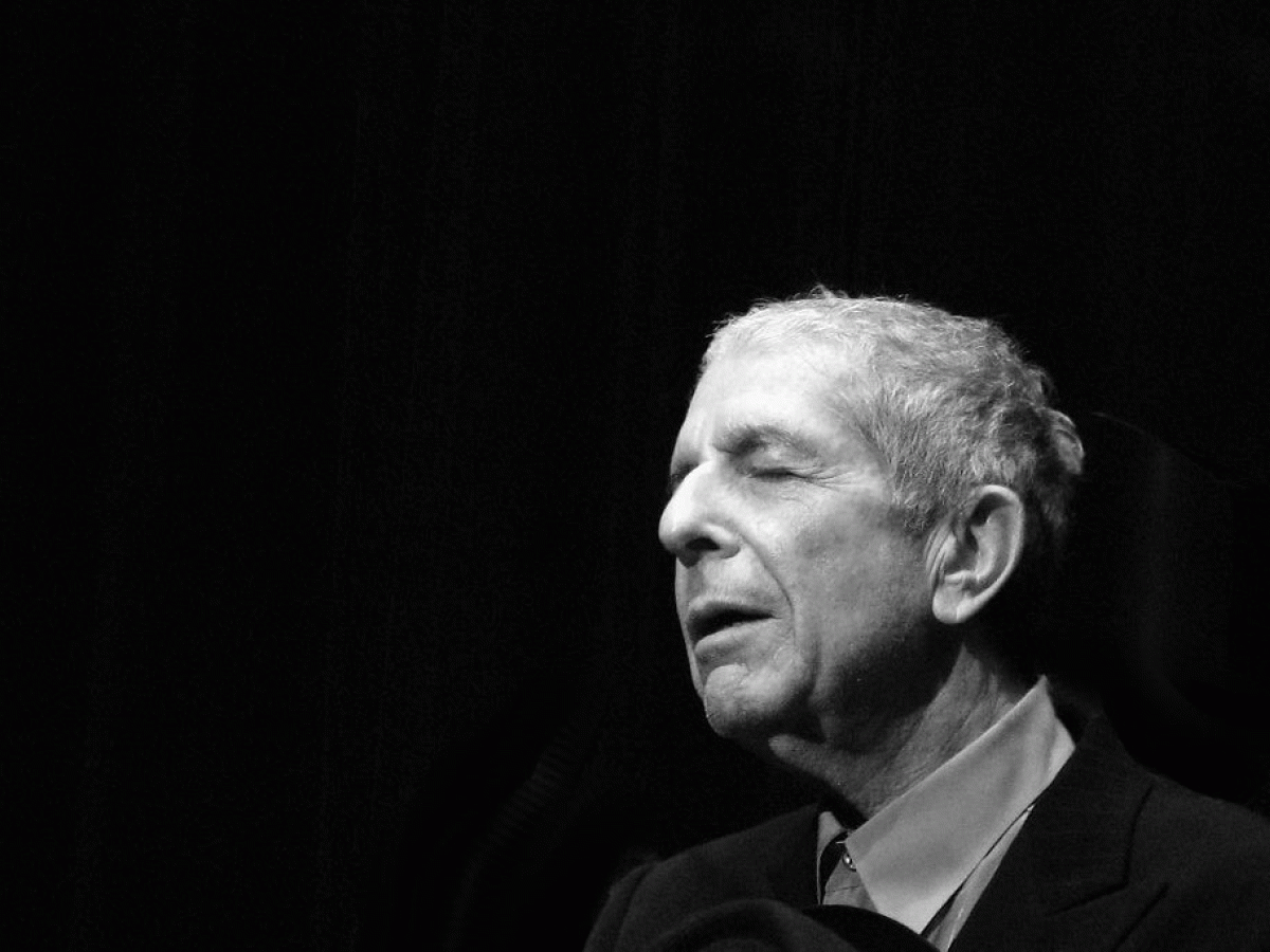 A black and white photo shows, singer Leonard Cohen to the right hand side, eyes closed and head inclined slightly upwards.