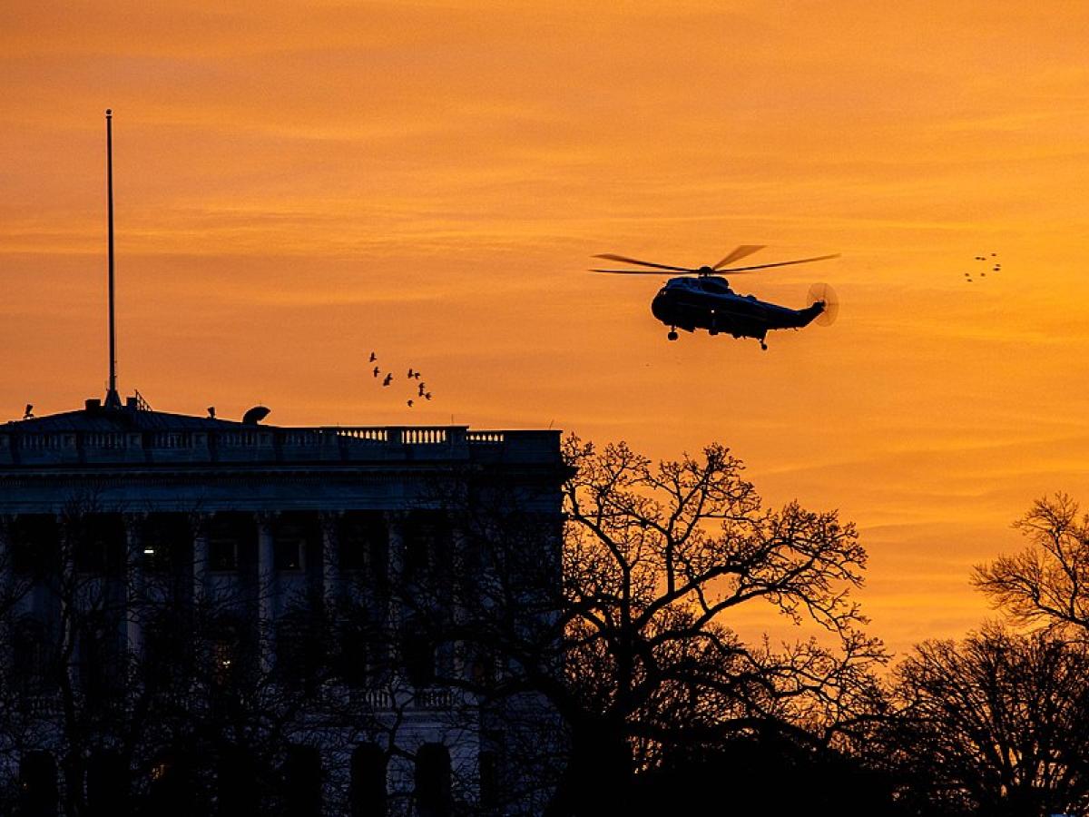 Silhoutted by a sun rise, a helicopter flies over The White House
