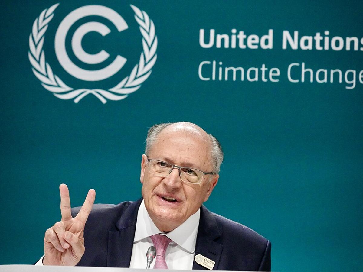 A speaker holds two fingers up while sitting in front of a backdrop reading 'United Nations Climate Change.