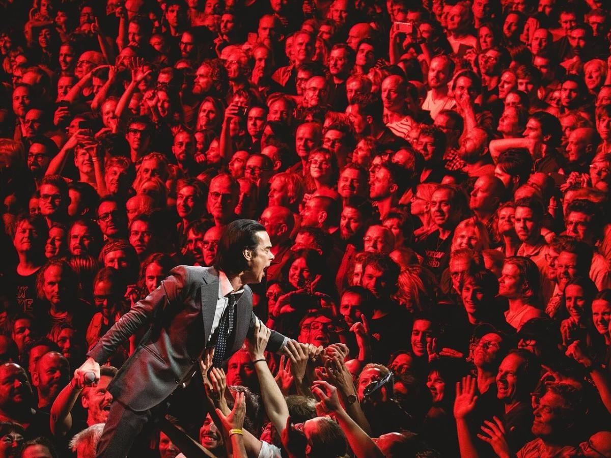 A rock star prowls the stage while behind hundred of faces tined red star.