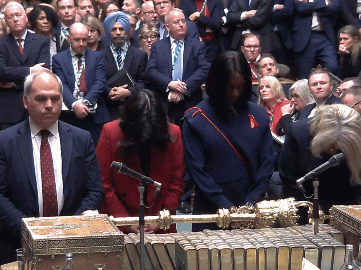 Four MPs stand at a table with heads bowed.