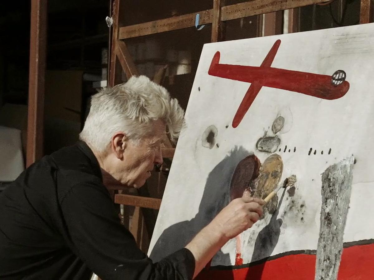 A man paints a canvas with red images.