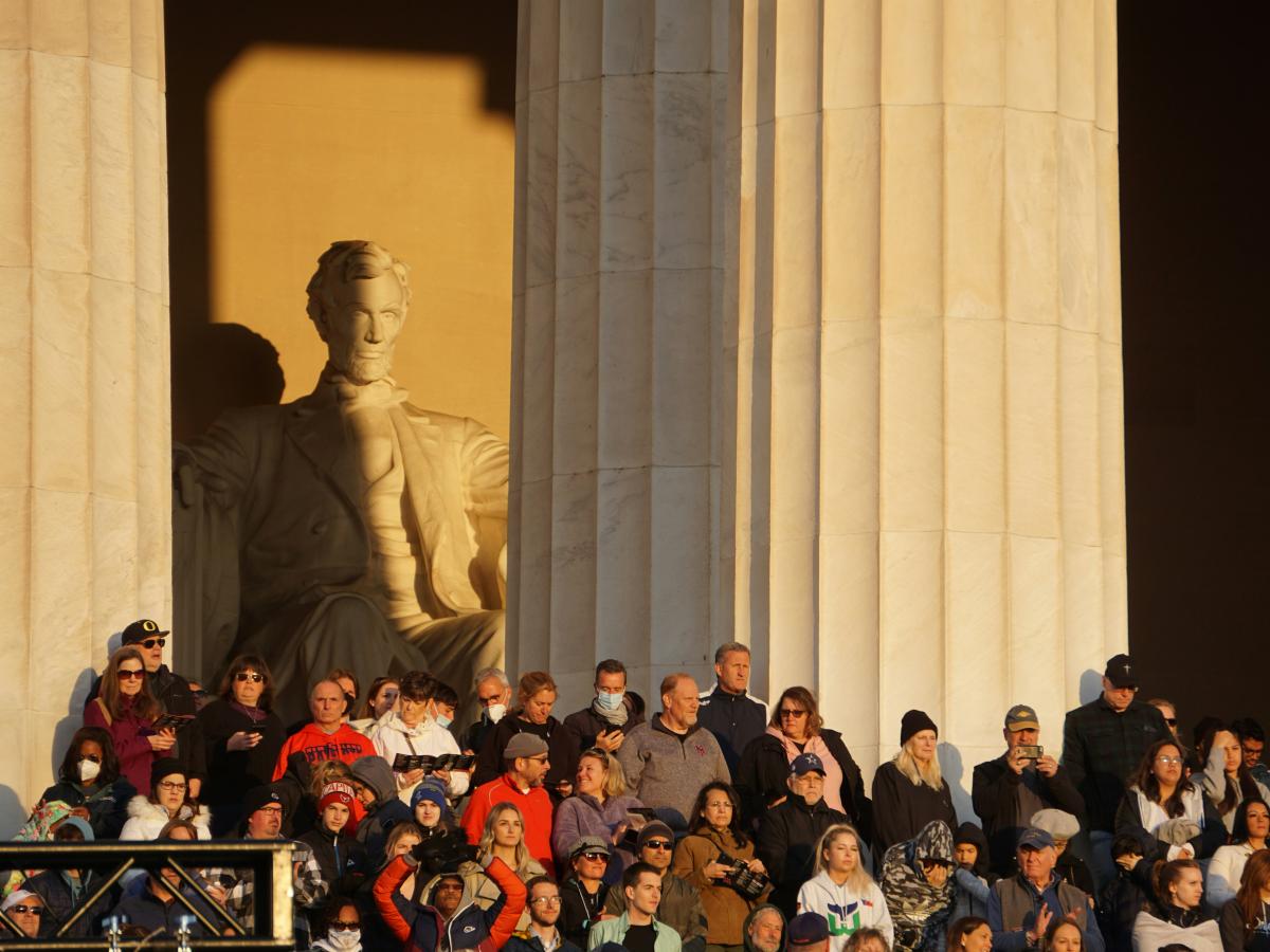 A crowd of people stand in the side steps of the Lincoln Memorial